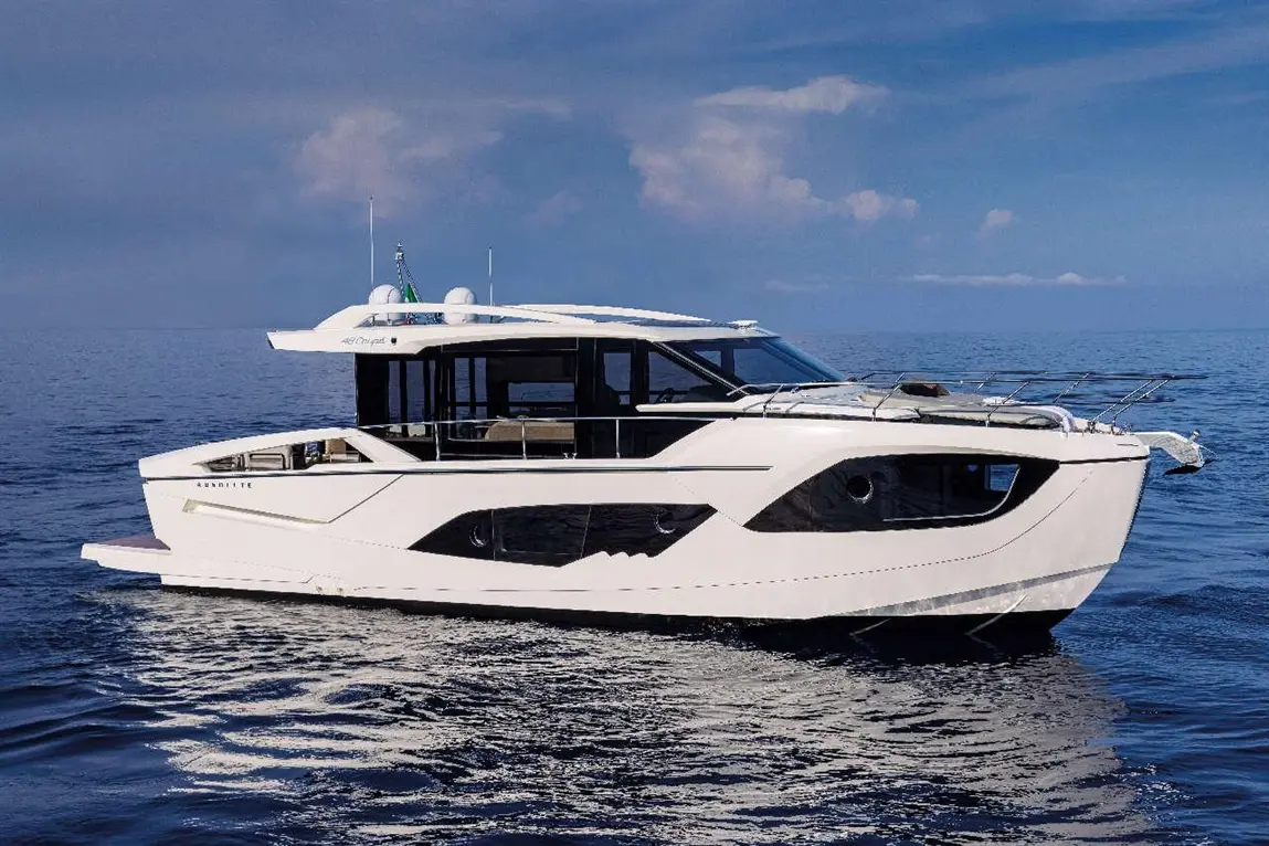 A sleek white motorboat navigates calm waters under a blue sky, featuring large windows and stylish design elements.